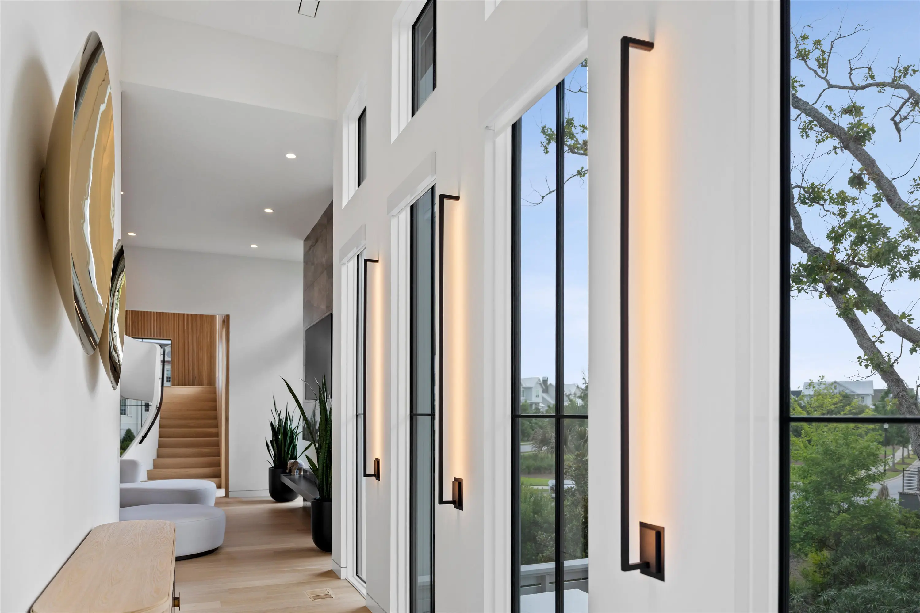 Modern wall-mounted lights brighten a sleek hallway with large windows.