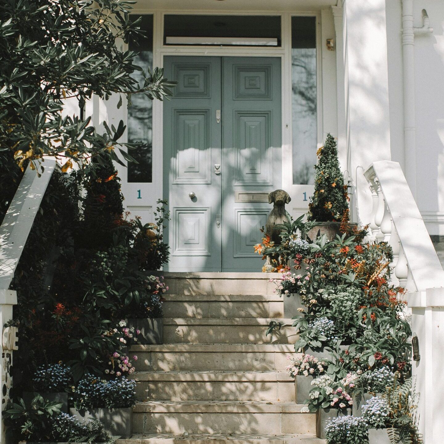 Stone steps leading to a pastel blue door surrounded by greenery.